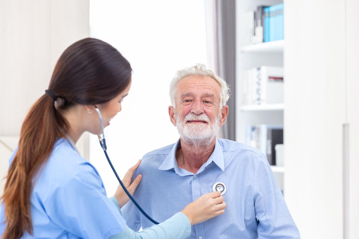 A nurse is listening to an older man 's heart with a stethoscope.