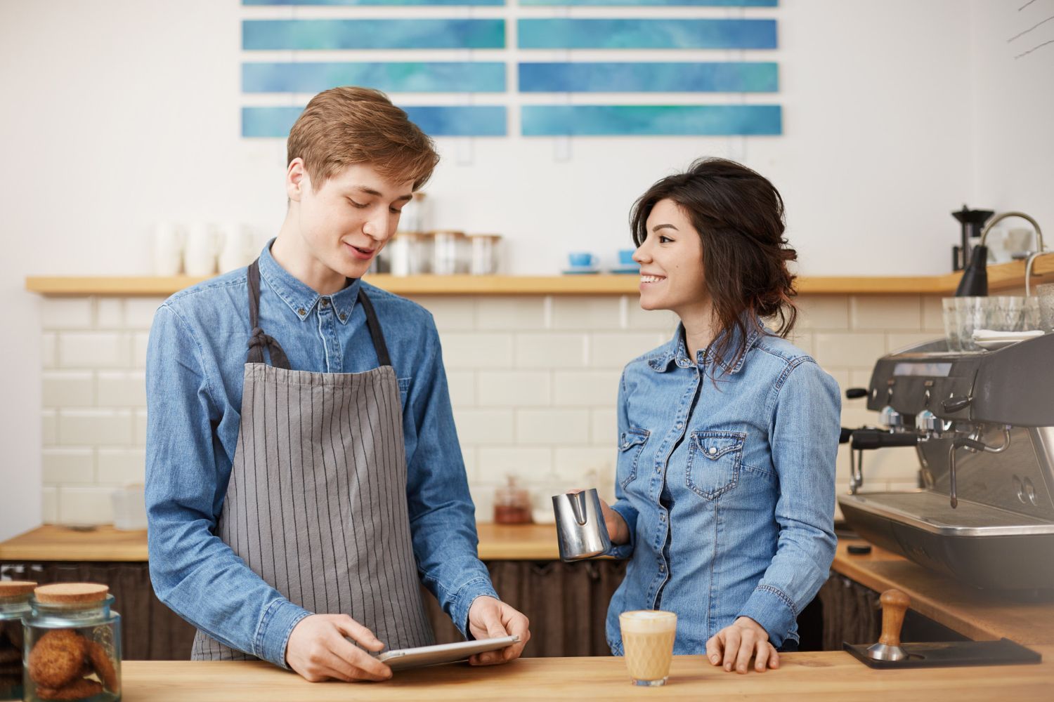 A man and a woman are standing in a kitchen looking at a tablet.