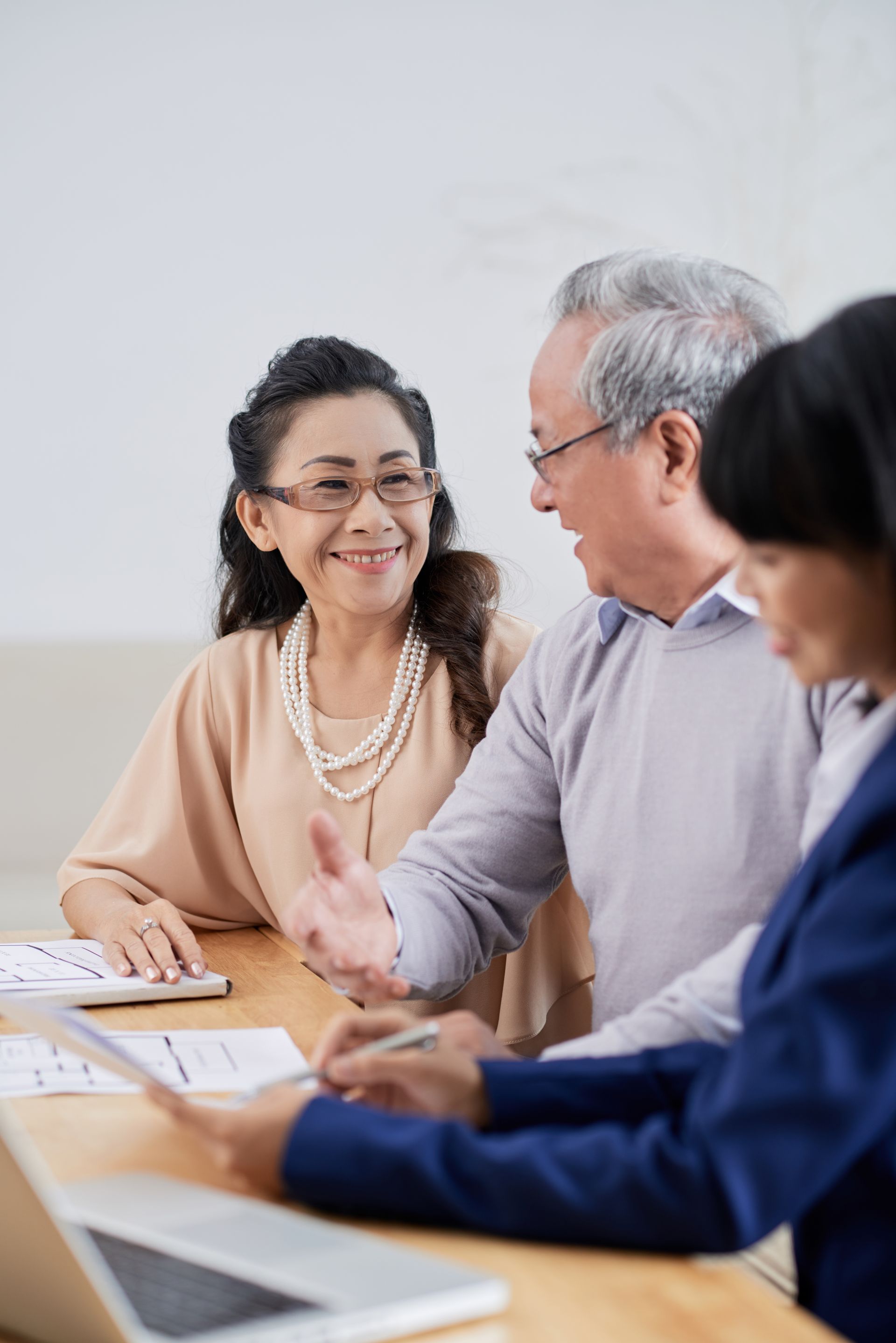 Three people sit at a wooden table reviewing documents during a professional meeting.