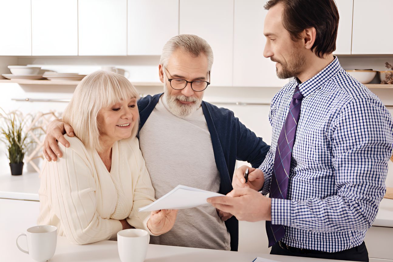 A Man Is Talking To An Elderly Couple In A Kitchen While Holding A Piece Of Paper — Grant Finance Solutions In Warwick, QLD