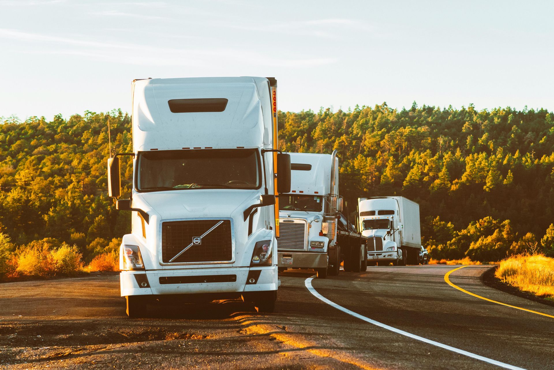 A row of semi trucks are driving down a curvy highway.