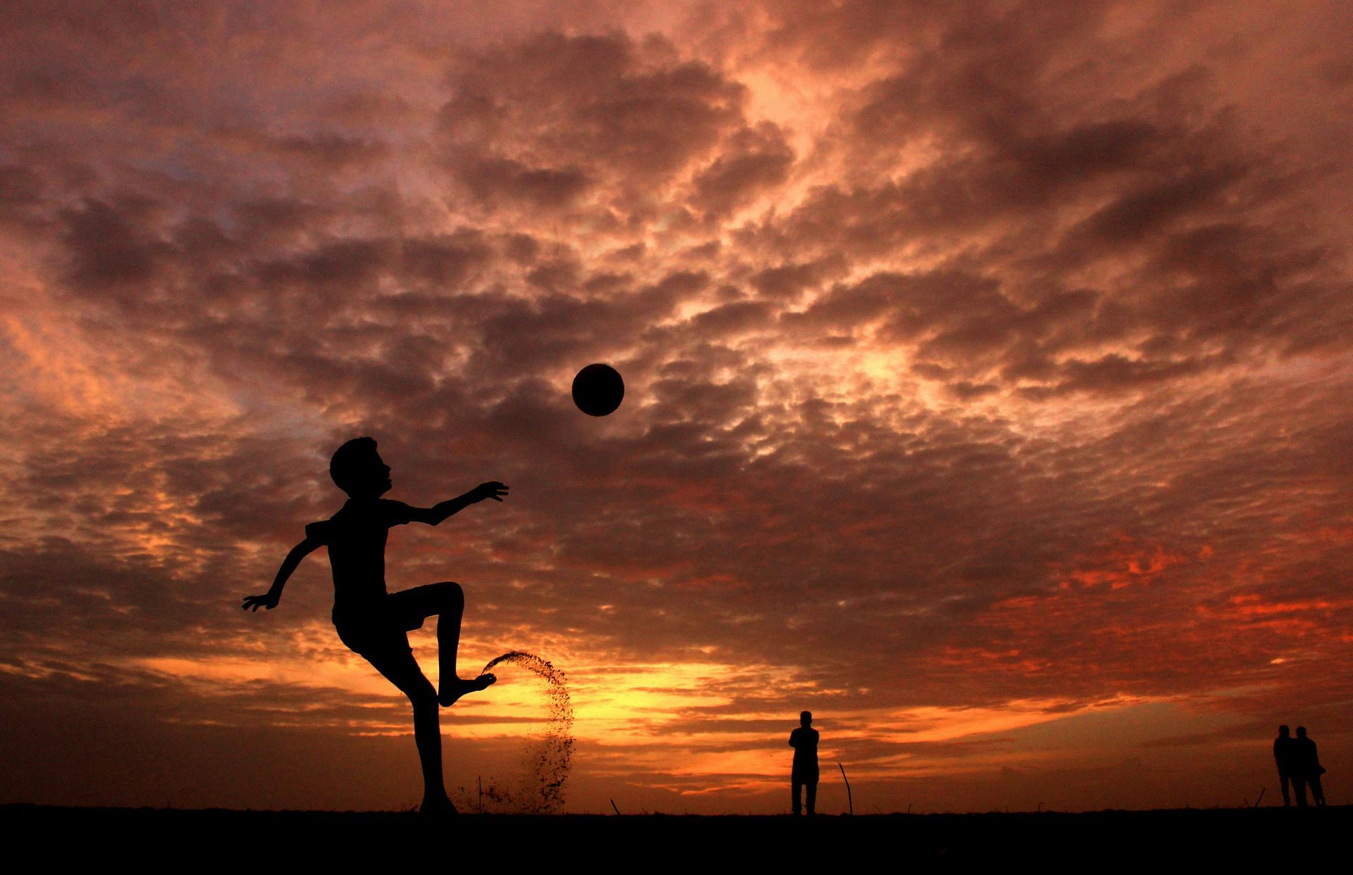 A silhouette of a person kicking a soccer ball at sunset.