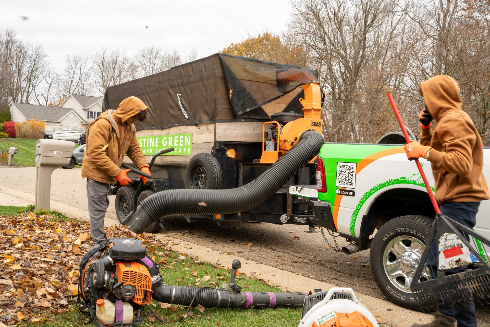 Two people using leaf blowers to load leaves into a truck with a leaf collection system.
