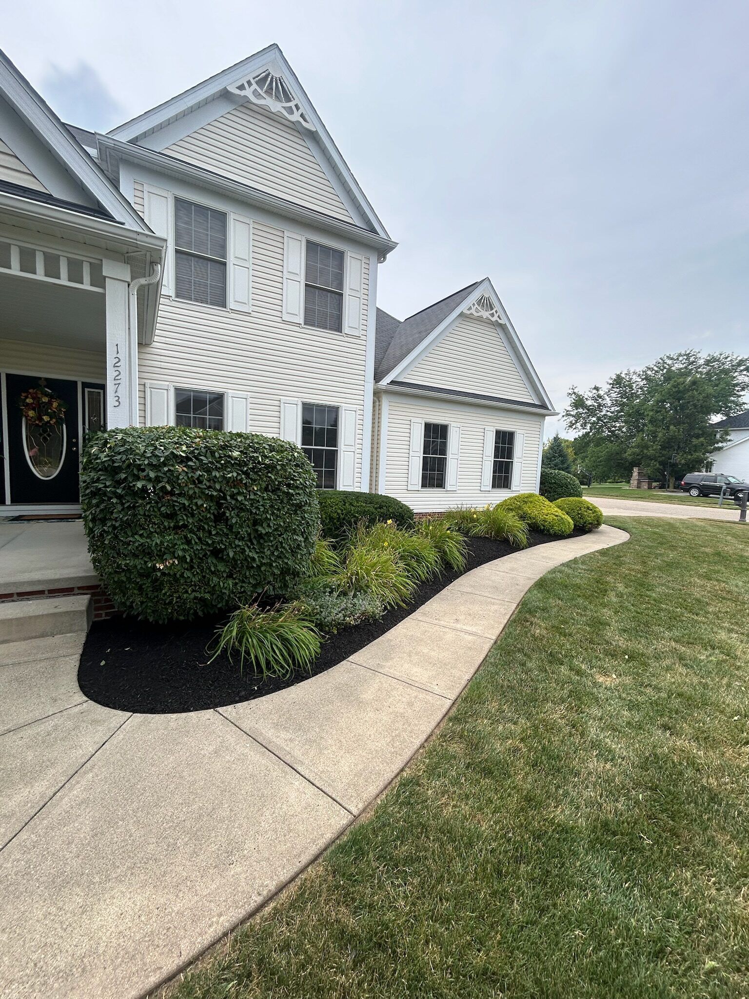 A white two-story house with landscaping. A curved walkway leads to the front door.