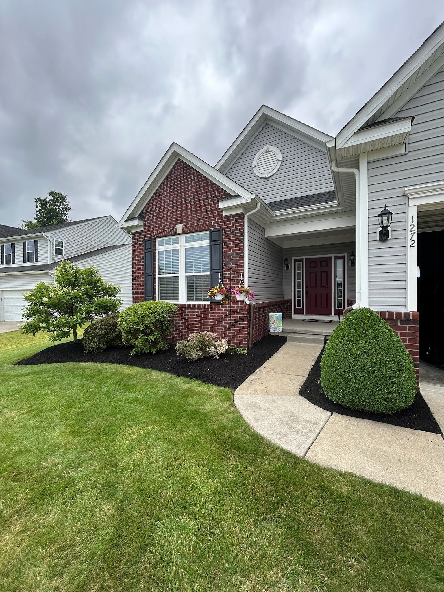Brick and gray home exterior with manicured lawn and landscaping. Cloudy sky.