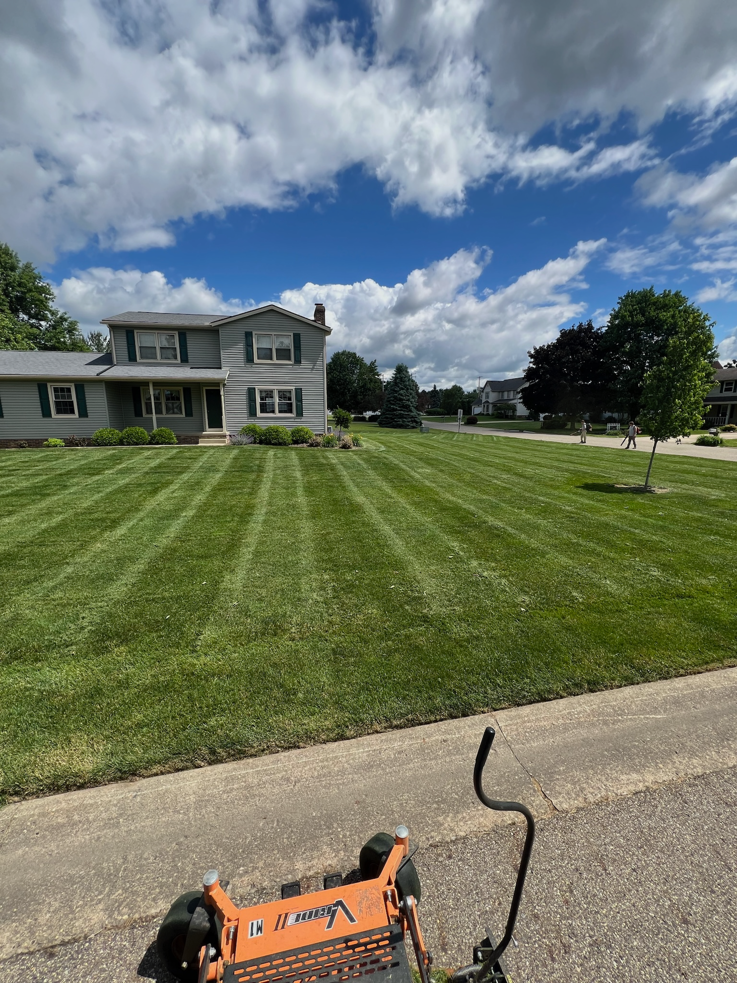 A lawn mower is sitting on the side of the road in front of a lush green lawn.