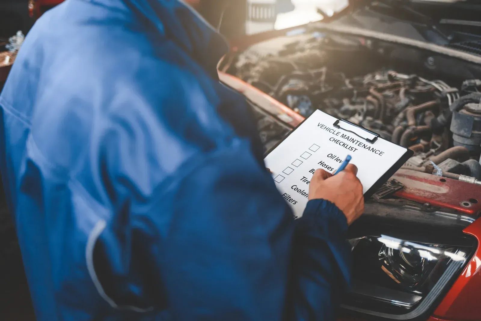 A mechanic is writing on a clipboard while working on a car.