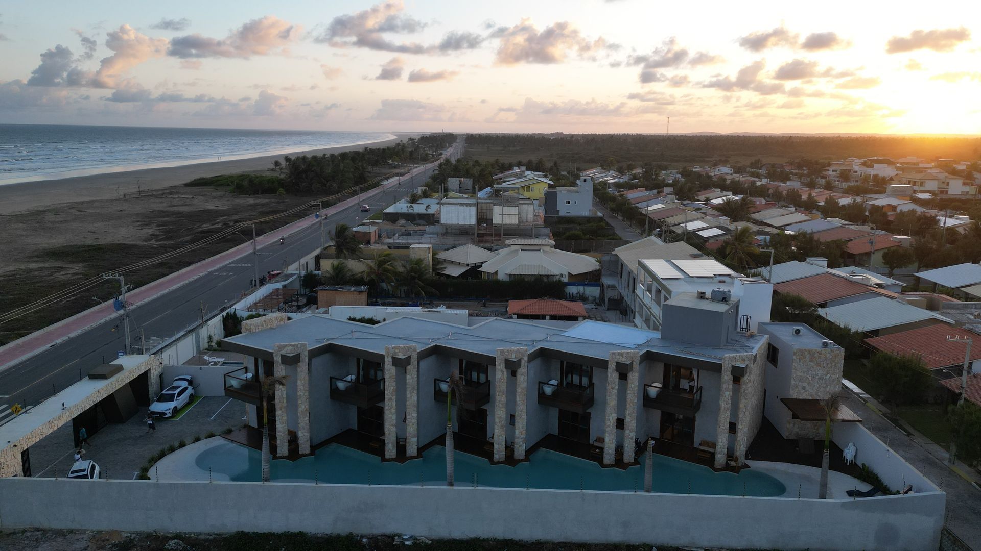 Uma vista aérea de um grande edifício próximo ao oceano ao pôr do sol.