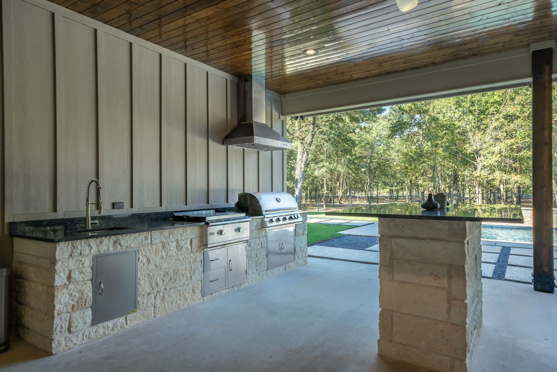 A large outdoor kitchen with a grill , sink , and sliding glass doors.