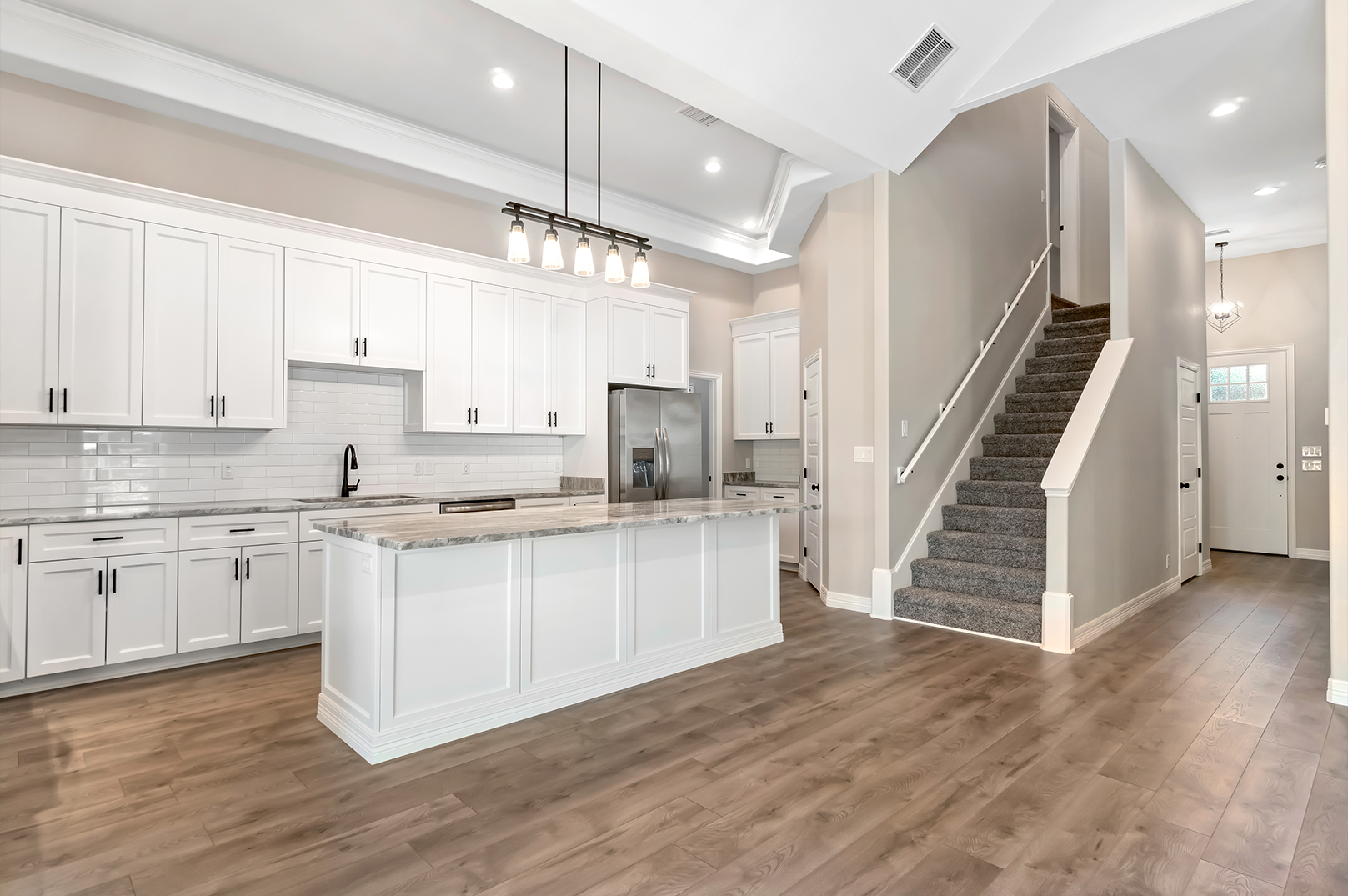 A kitchen with a large island and stairs leading up to the second floor.