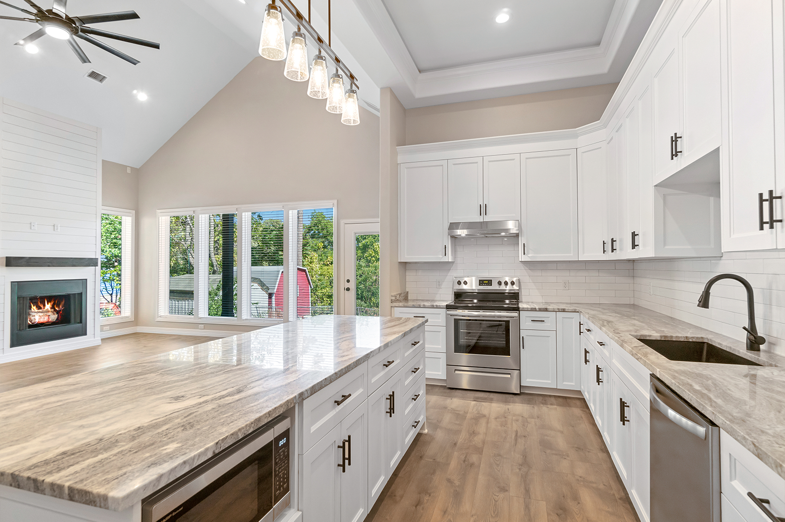 A kitchen with white cabinets , granite counter tops , stainless steel appliances and a fireplace.