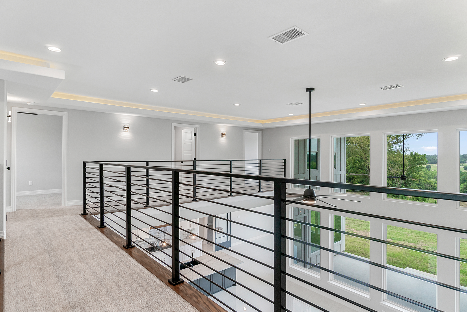 A hallway in a house with a railing and a ceiling fan.