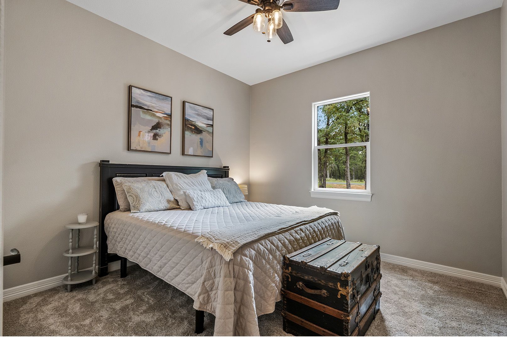 A bedroom with a bed , a trunk , a window and a ceiling fan.