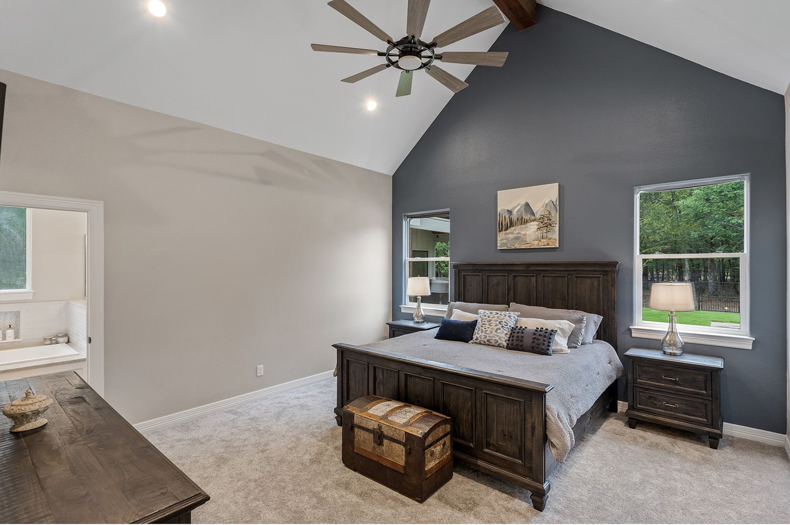 A bedroom with a vaulted ceiling , a king size bed , a dresser and a ceiling fan.