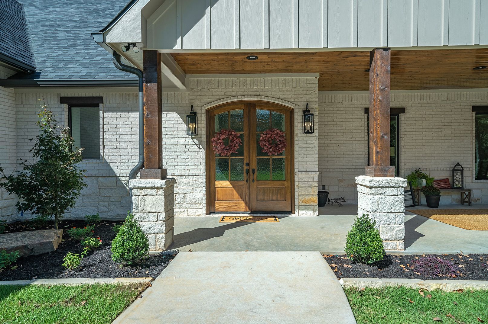 A white brick house with a wooden door and a concrete walkway leading to it.