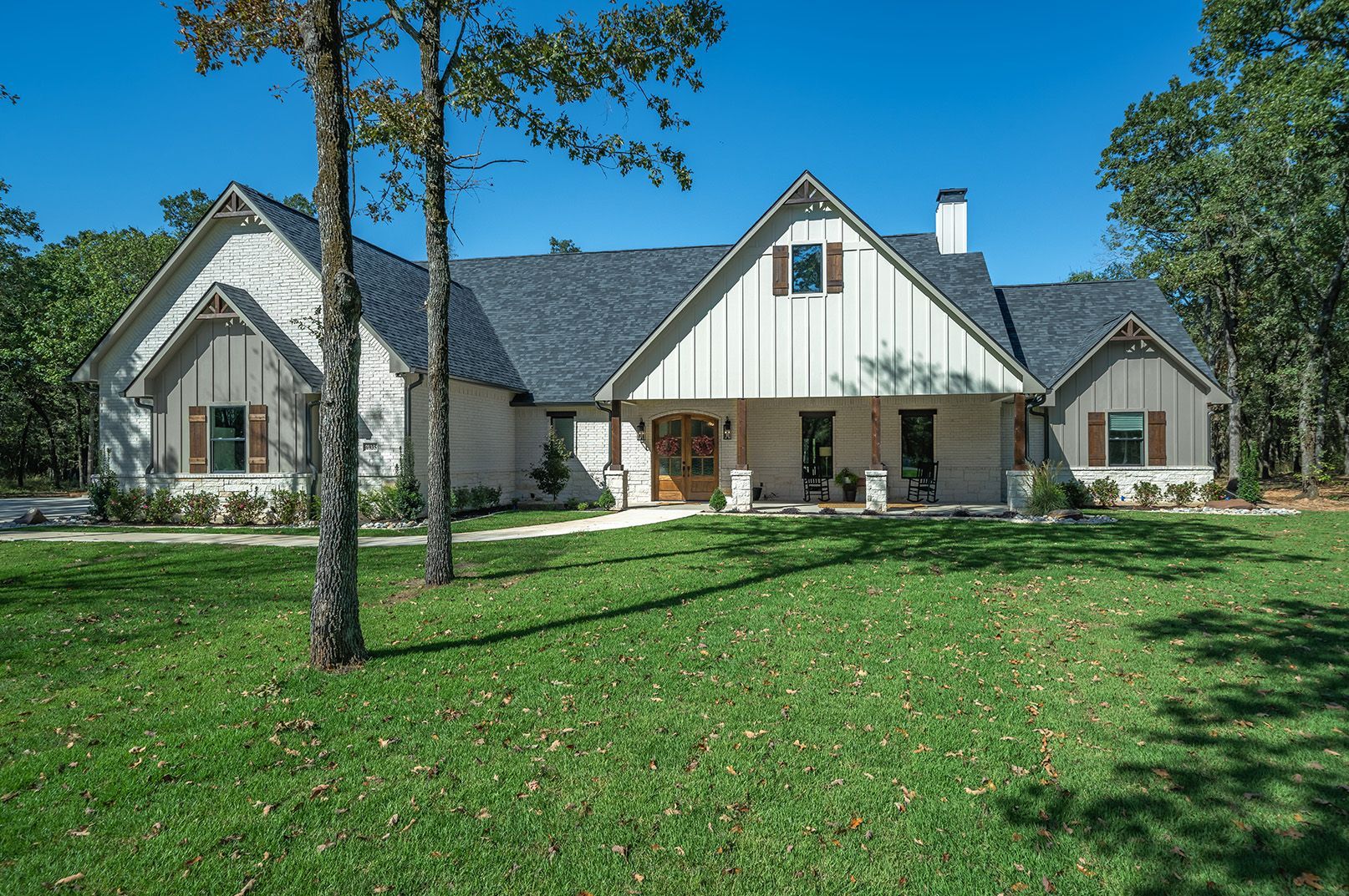 A large white house with a gray roof is sitting on top of a lush green lawn.