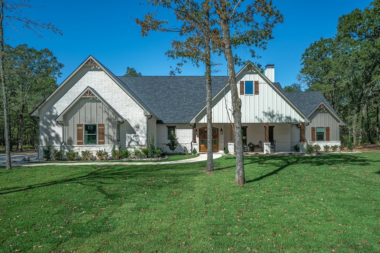 A large white house with a gray roof is sitting in the middle of a lush green field.