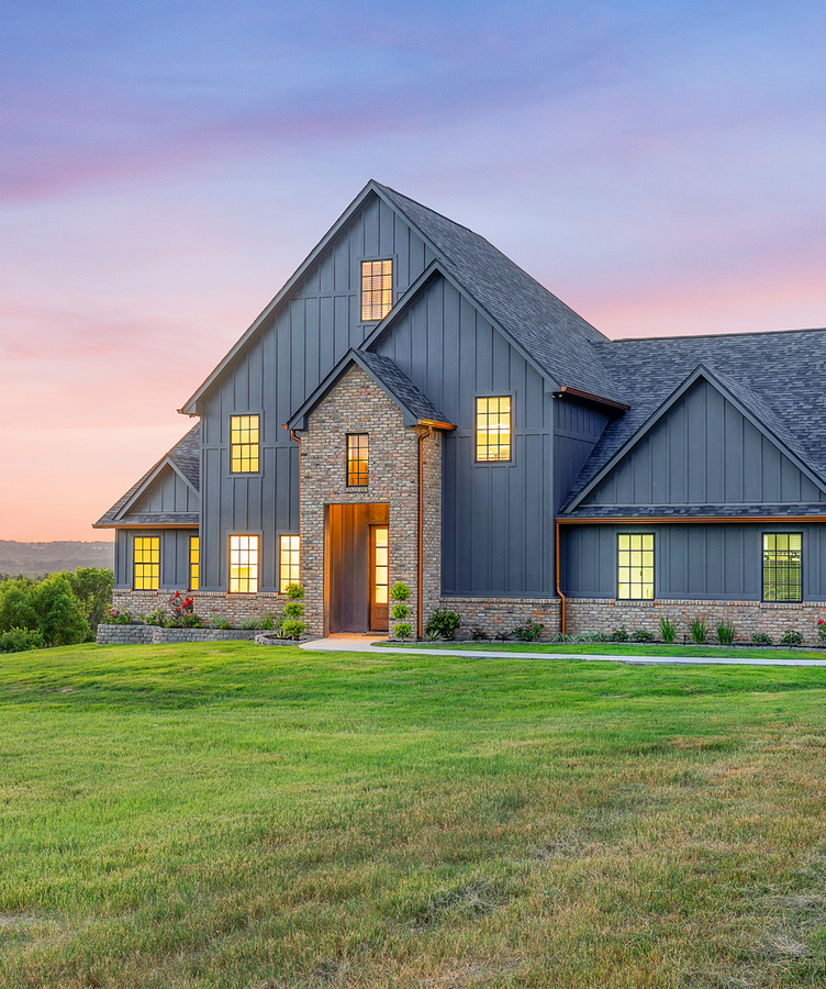 A large house with a lot of windows is sitting on top of a lush green field.