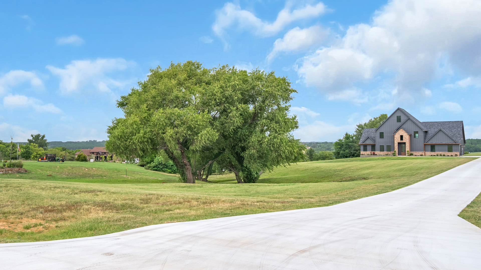 A large house is sitting on top of a lush green field next to a dirt road.