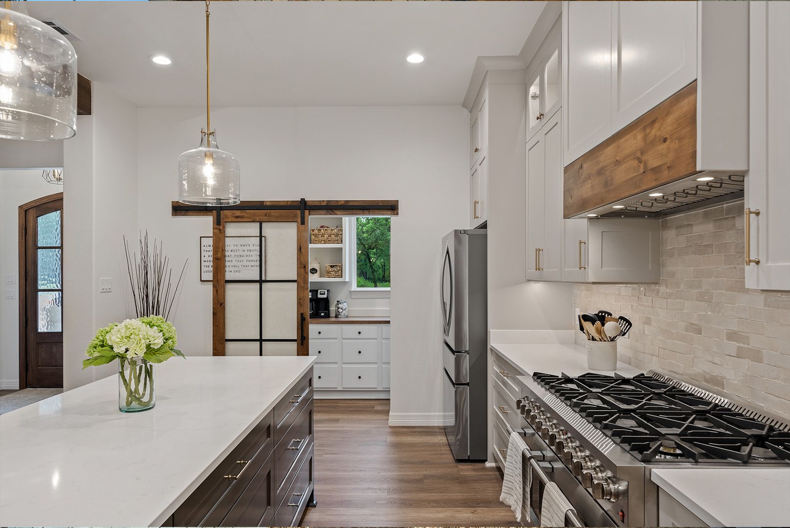 A kitchen with white cabinets , a stove , a refrigerator , and a sliding barn door.