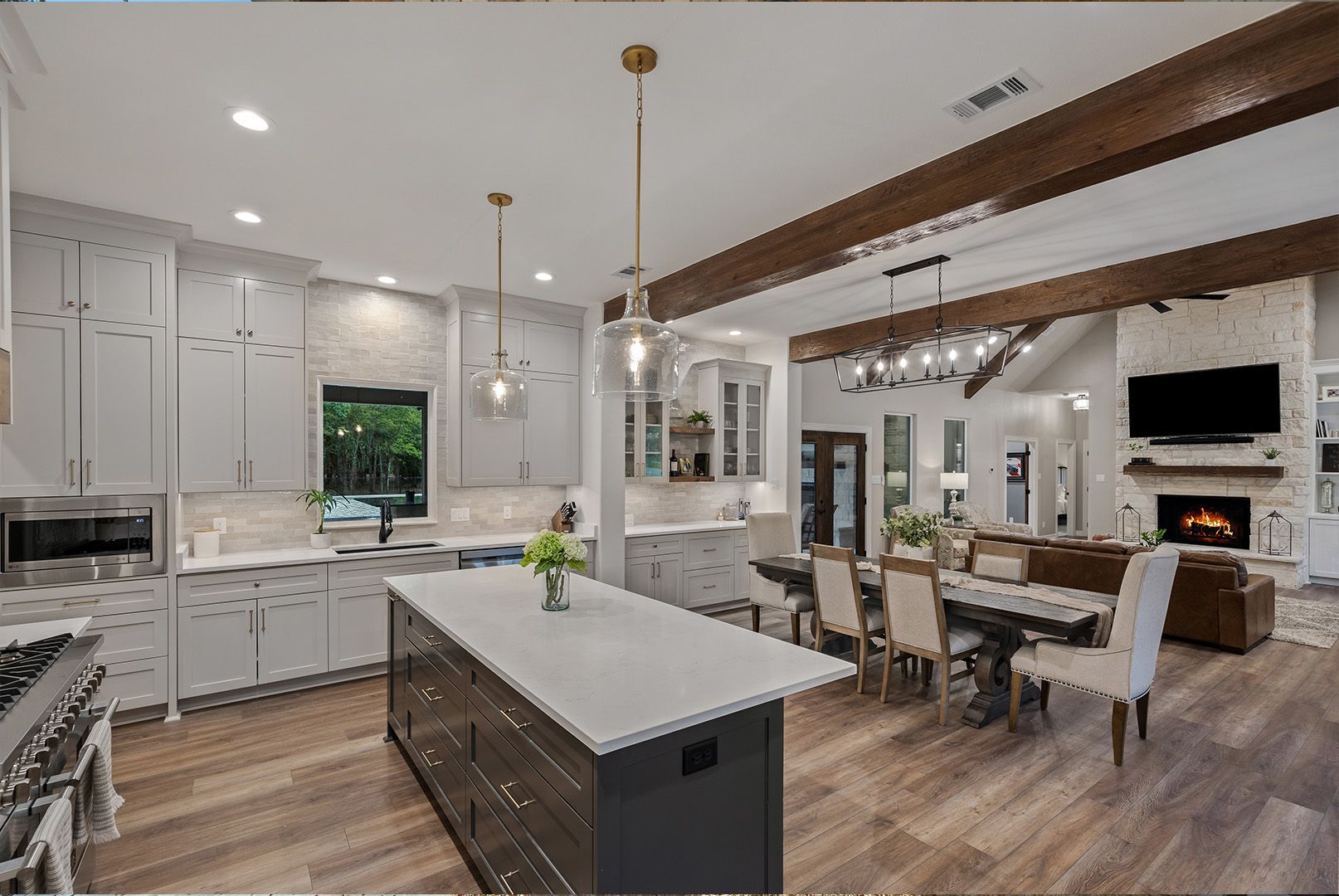A kitchen with white cabinets , a large island , a dining table and chairs , and a fireplace.