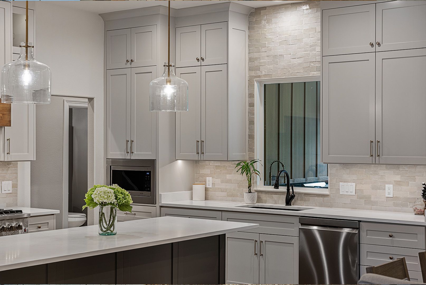 A kitchen with gray cabinets , white counter tops , stainless steel appliances and a large island.