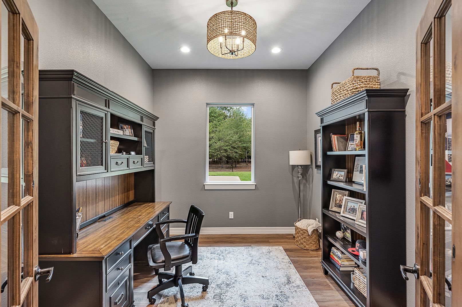 A home office with a desk , chair , shelves and a window.