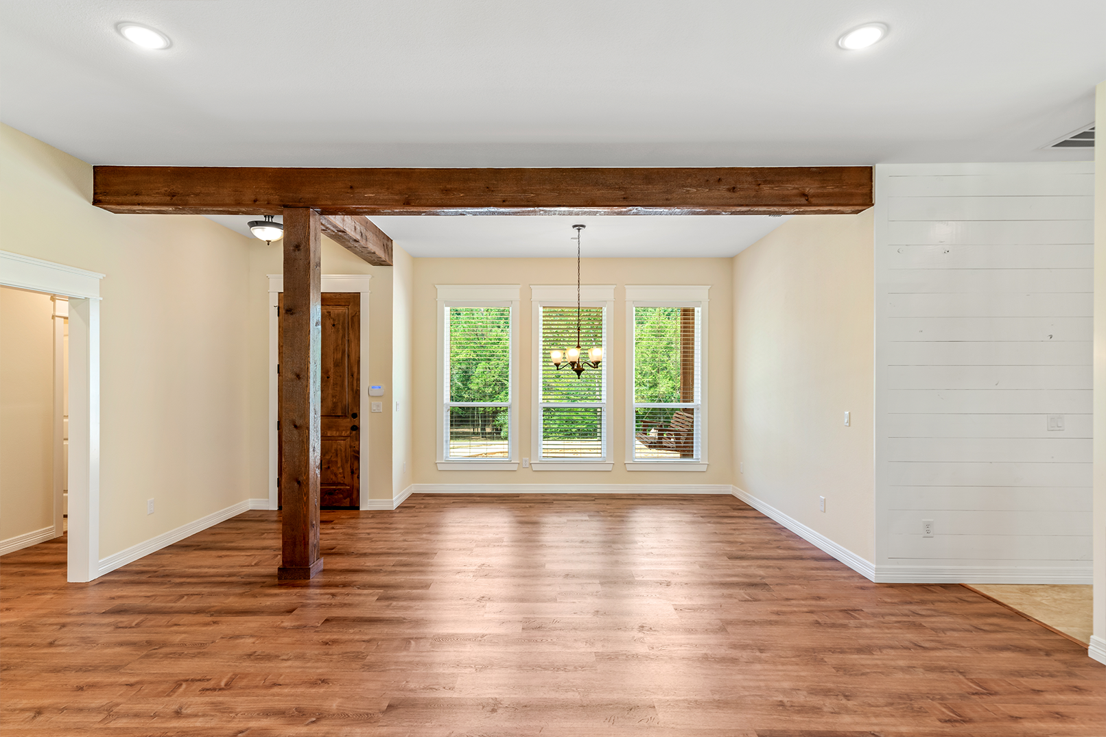 An empty living room with hardwood floors and a wooden beamed ceiling.
