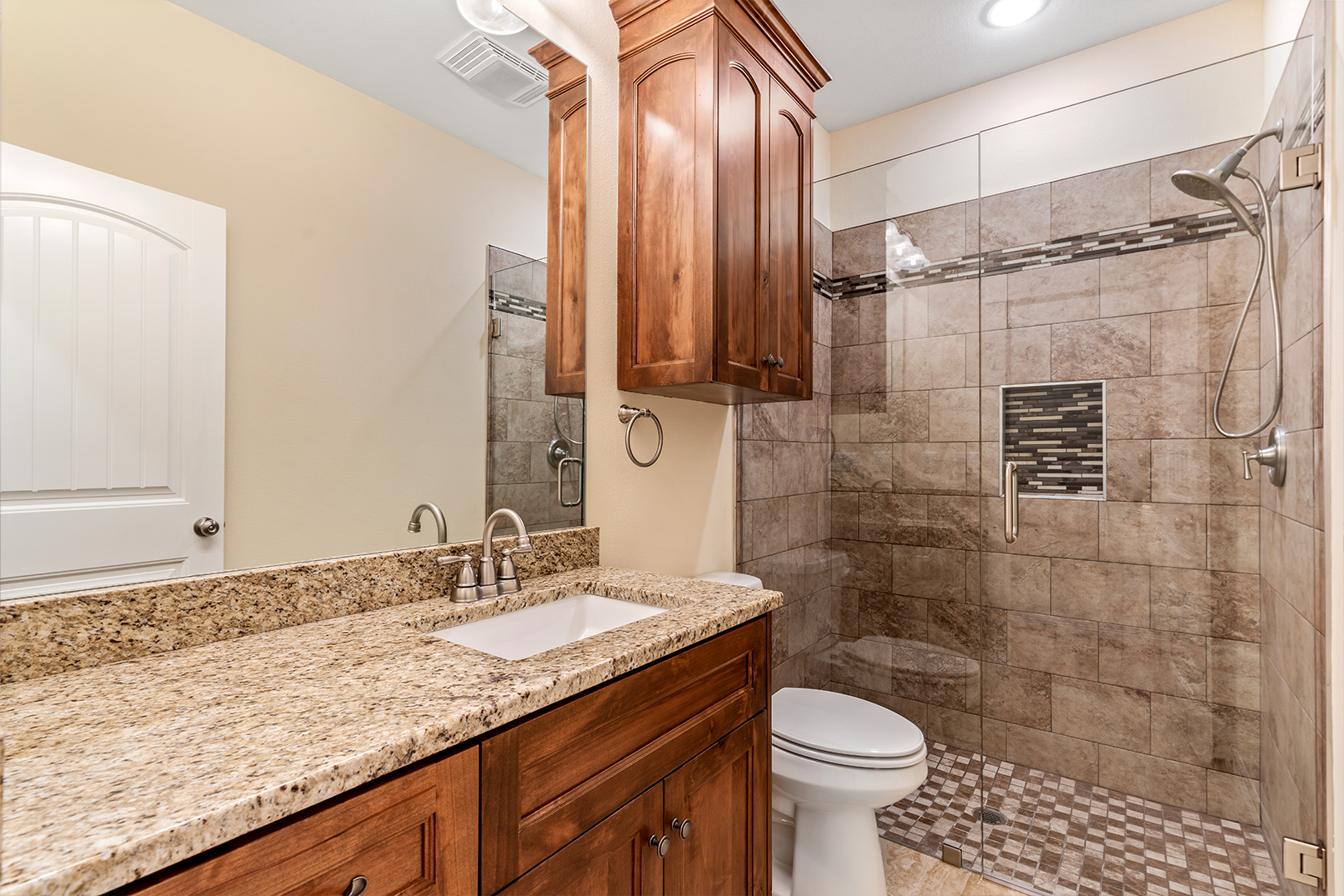 A bathroom with a walk in shower , sink , toilet and mirror.