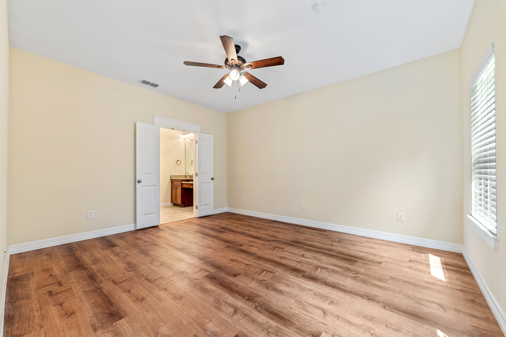 An empty bedroom with hardwood floors and a ceiling fan.