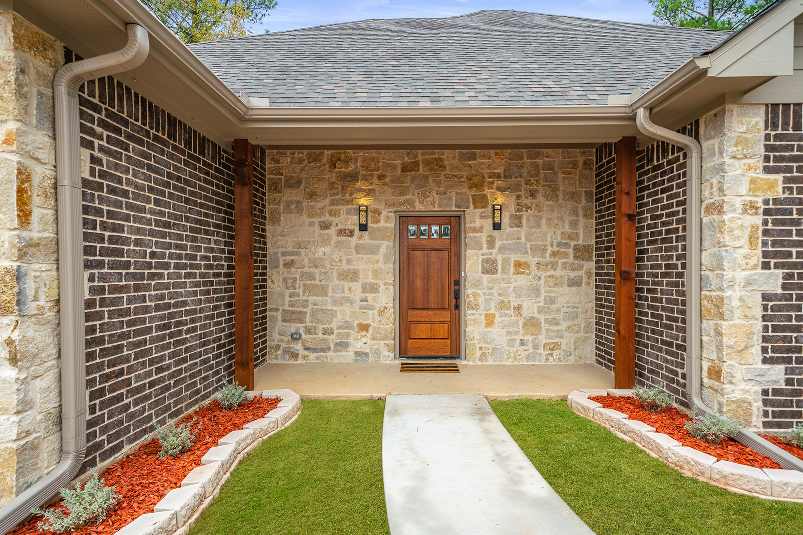 A brick house with a wooden door and a concrete walkway leading to it.