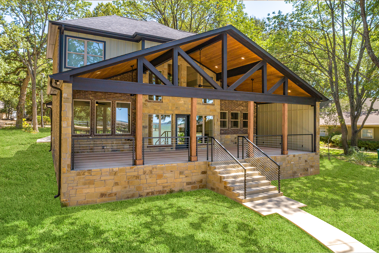 A large house with a large porch and stairs is sitting on top of a lush green hillside.