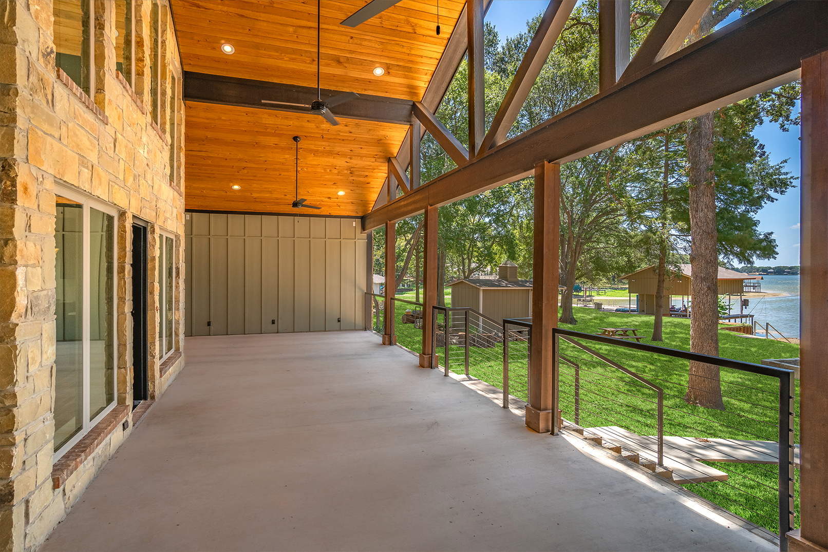 A large covered porch with a wooden ceiling and a view of a lake.