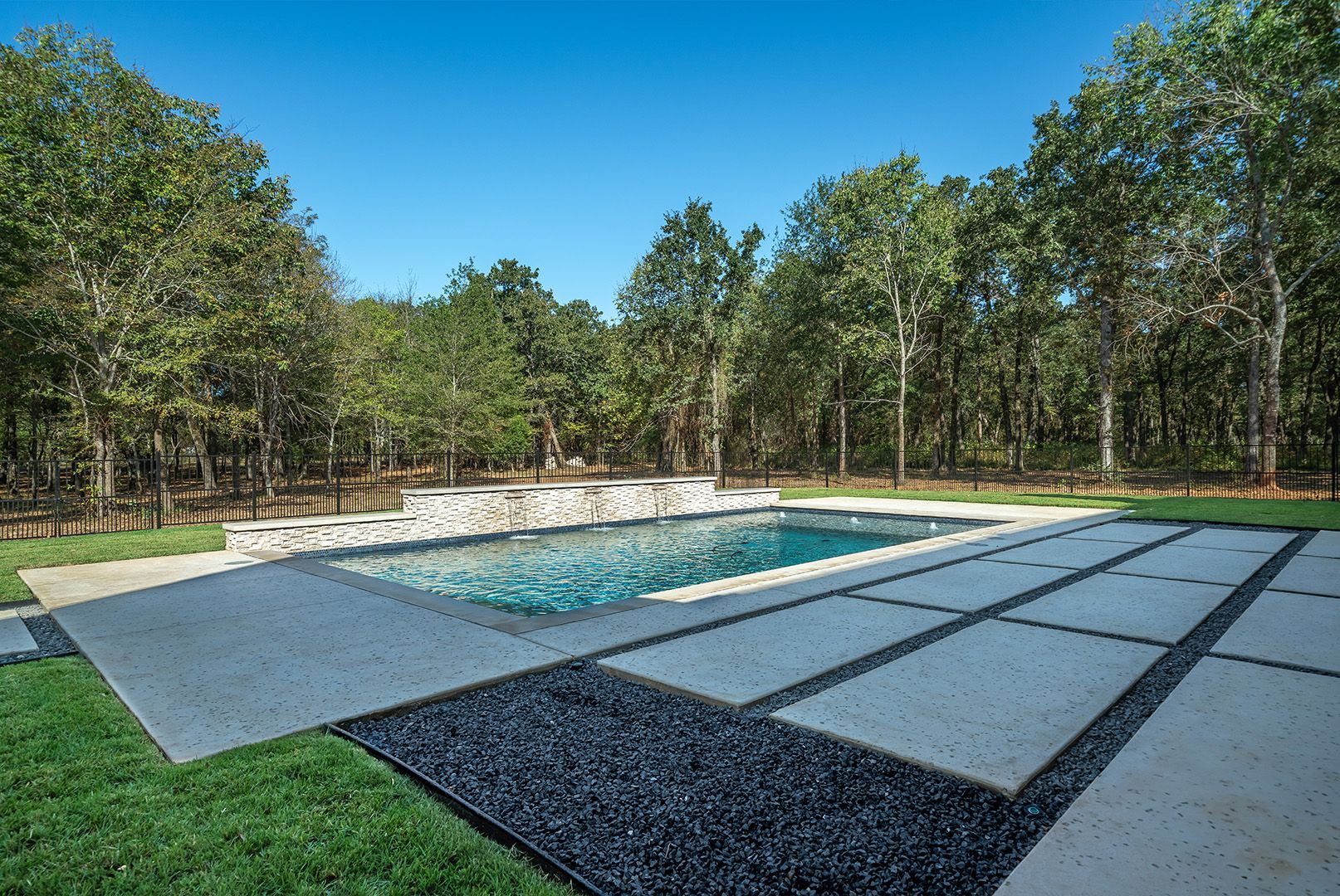 There is a large swimming pool in the backyard surrounded by trees.