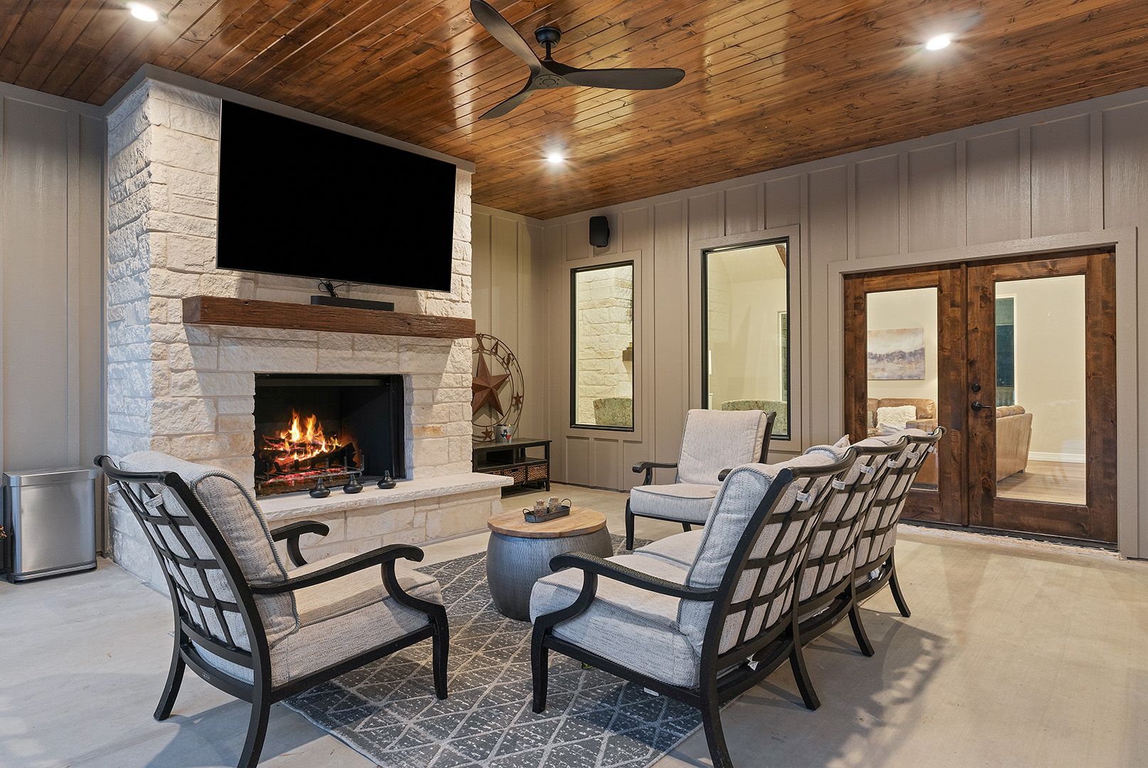 A living room with a fireplace , chairs , a flat screen tv and a ceiling fan.