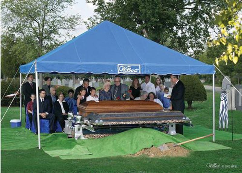 a group of people are gathered around a coffin under a blue tent