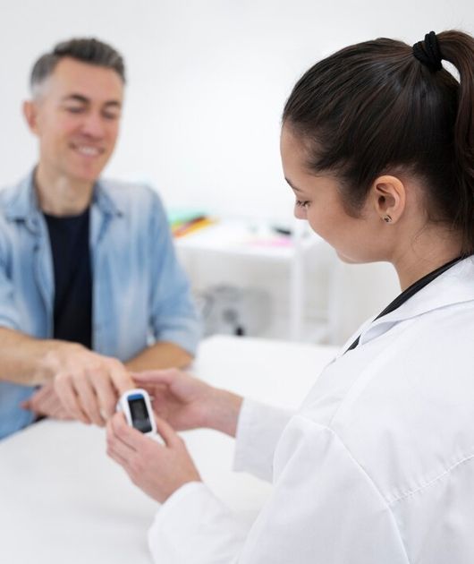 Clinician holding a pulse oximeter while checking a smiling patient’s finger in a bright clinic