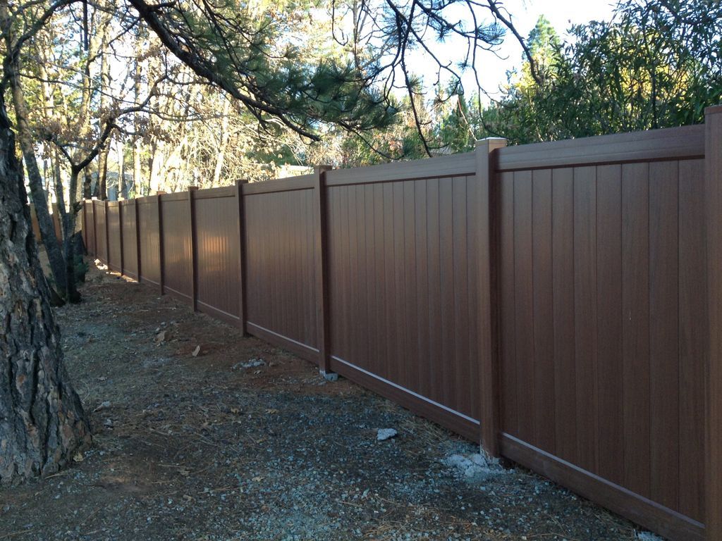 A brown wooden fence is surrounded by trees and dirt.