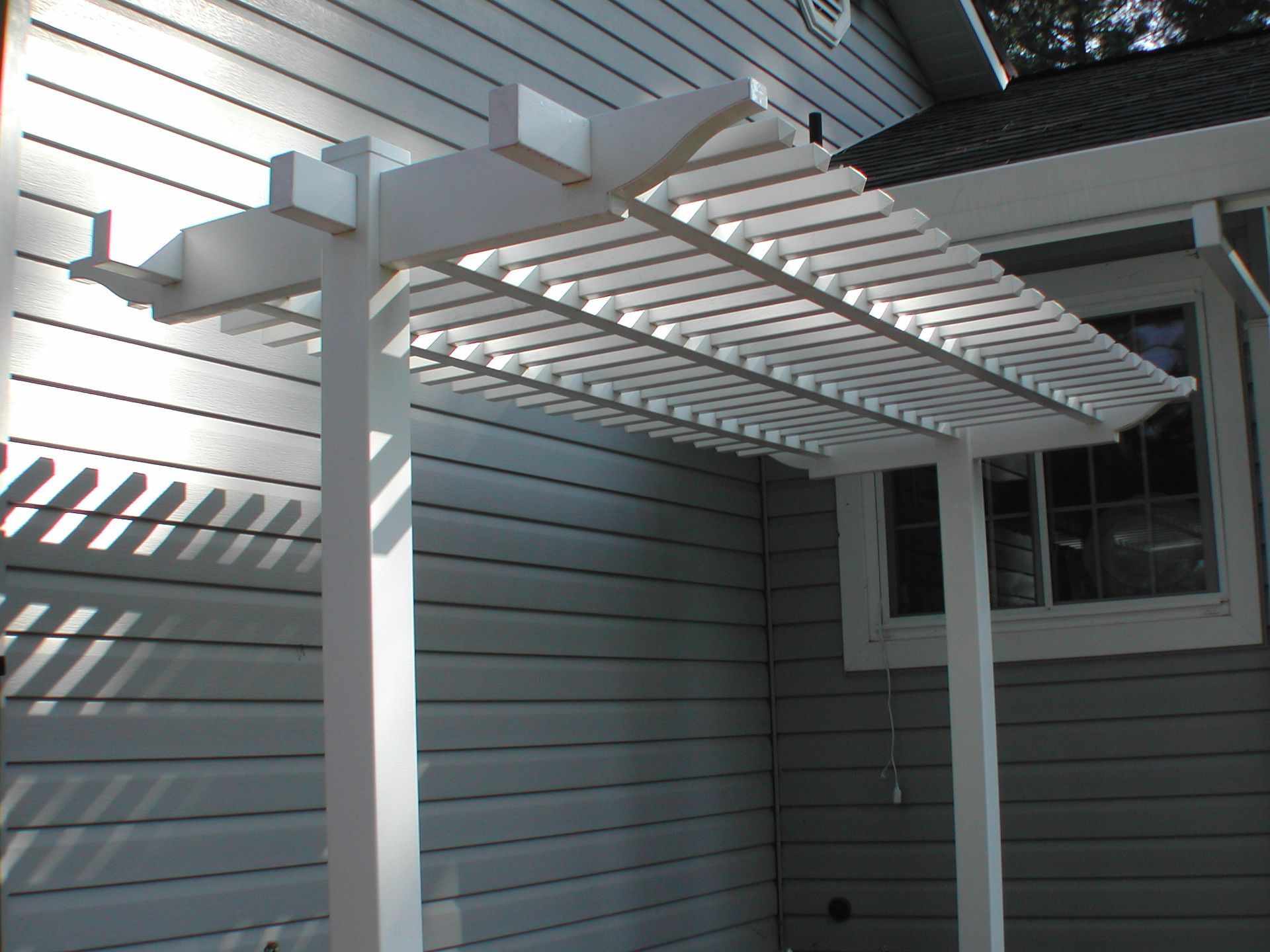 A white pergola is attached to the side of a house