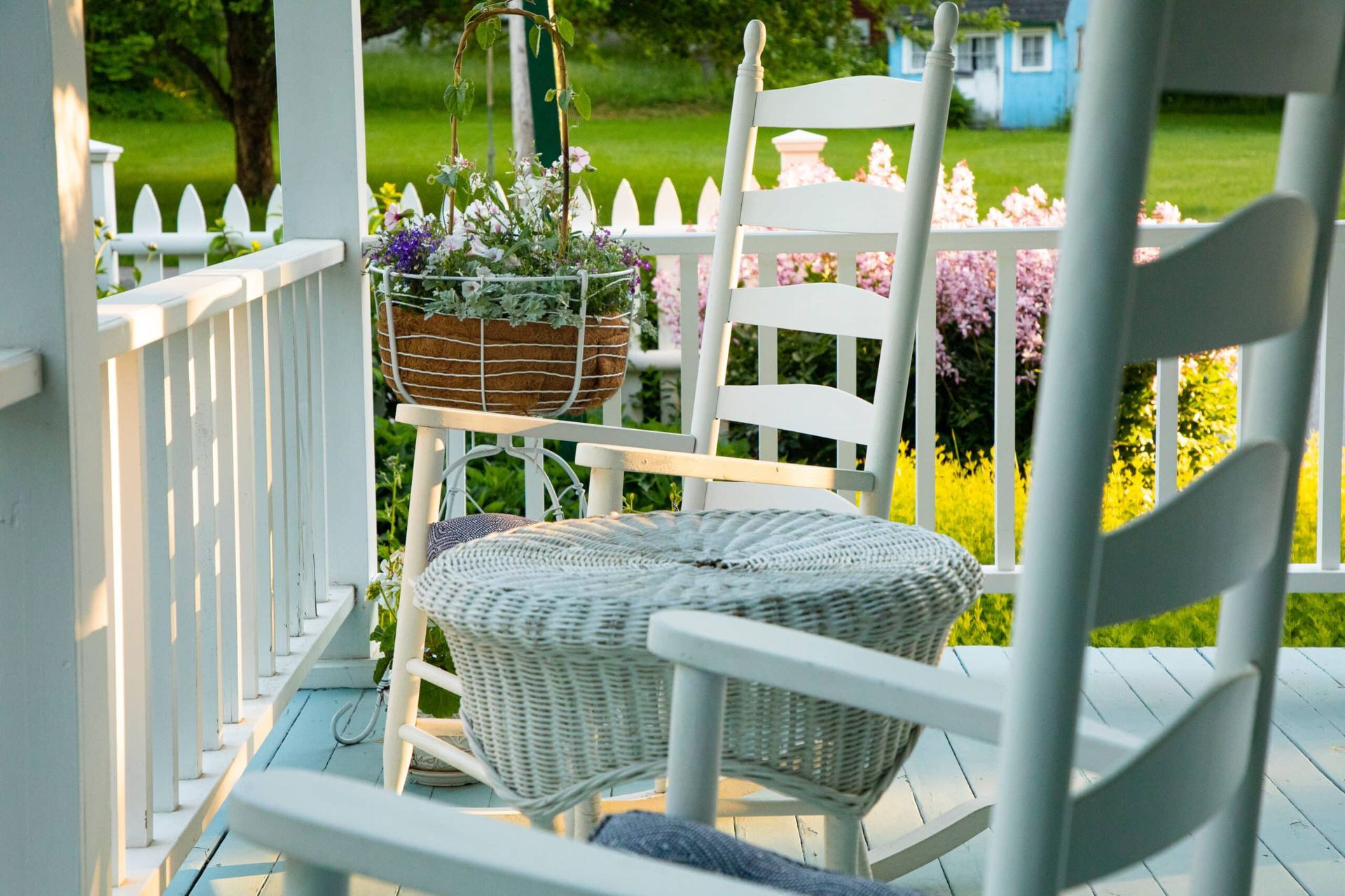 Two white rocking chairs and a wicker table on a porch