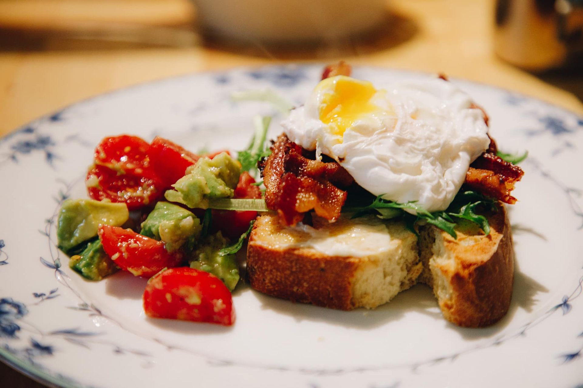 A plate of food with eggs , bacon , avocado and tomatoes on a table.