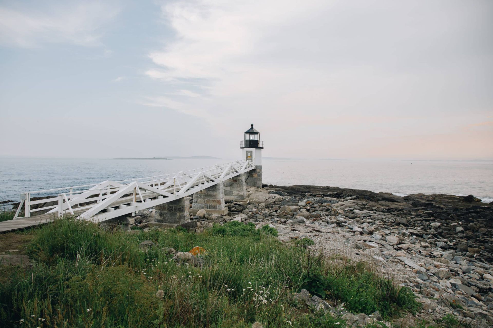 A lighthouse on the shore of a rocky beach next to the ocean.