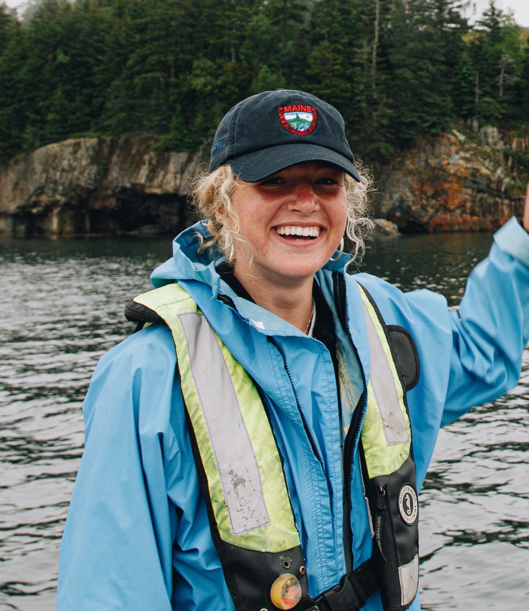 A woman wearing a life jacket and a hat is standing in the water.