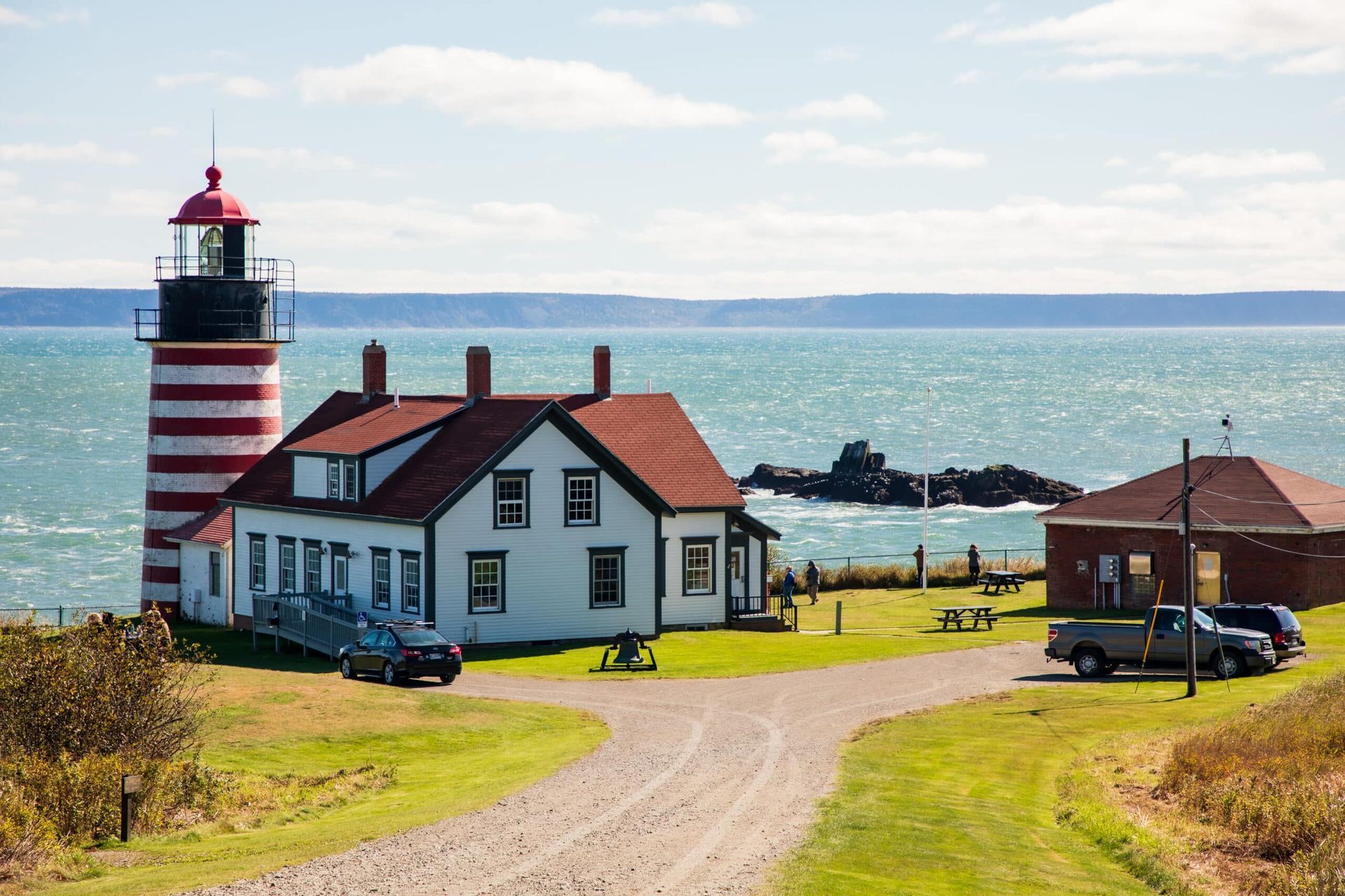 A lighthouse is sitting on top of a grassy hill next to the ocean.