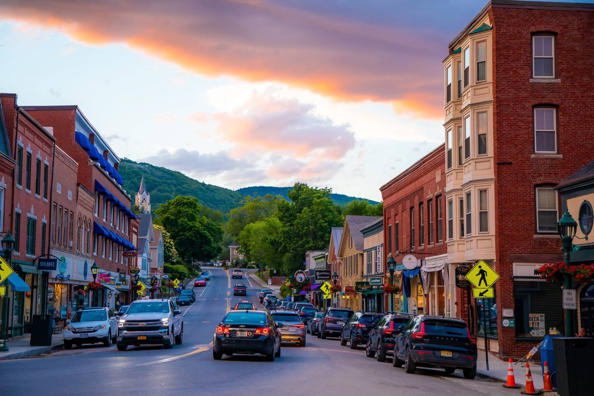 A busy street in a small town with cars driving down it.