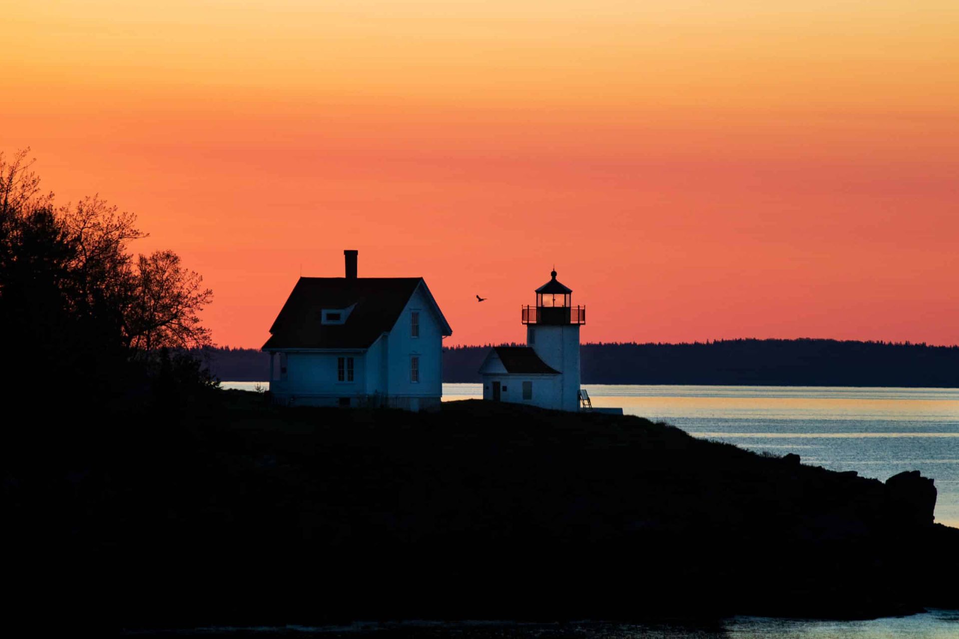 A lighthouse is sitting on top of a hill overlooking the ocean at sunset.