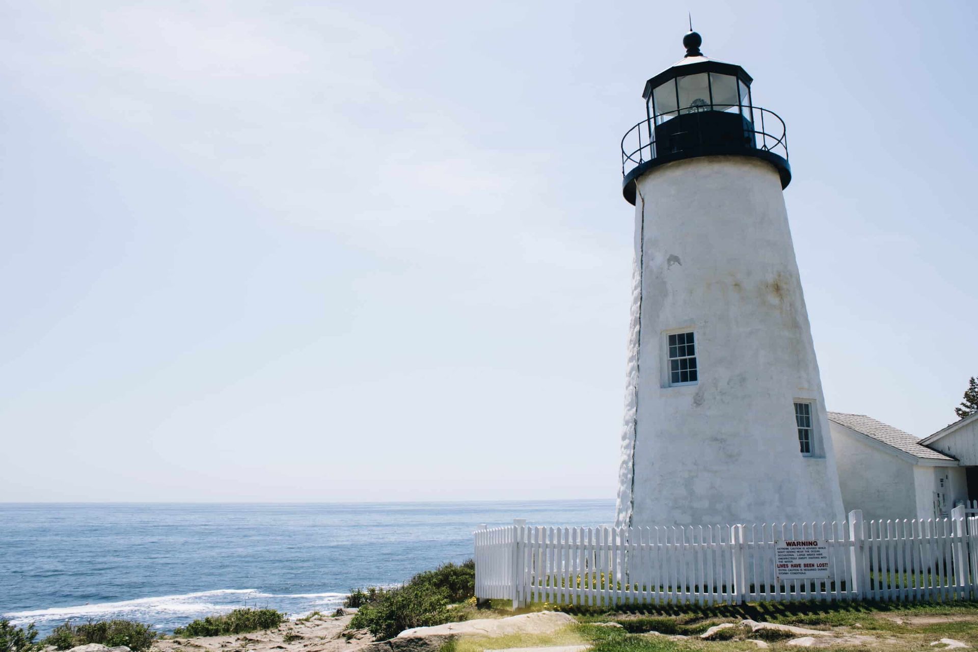 A white lighthouse sitting on top of a cliff overlooking the ocean.