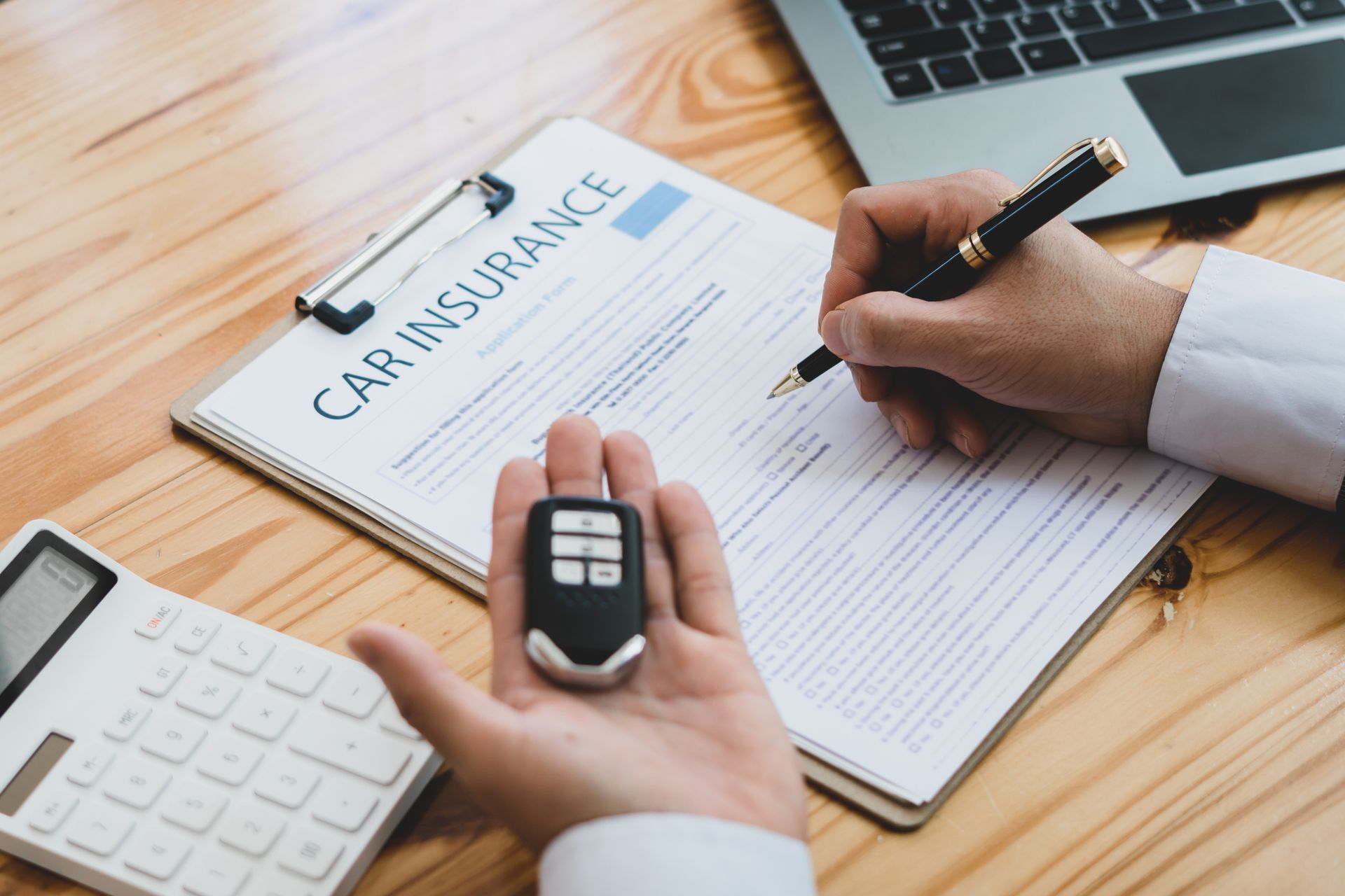 Man signing car insurance form with pen, holding car key, calculator and paperwork on desk. Man signing car insurance form with pen, holding car key, calculator and paperwork on desk.