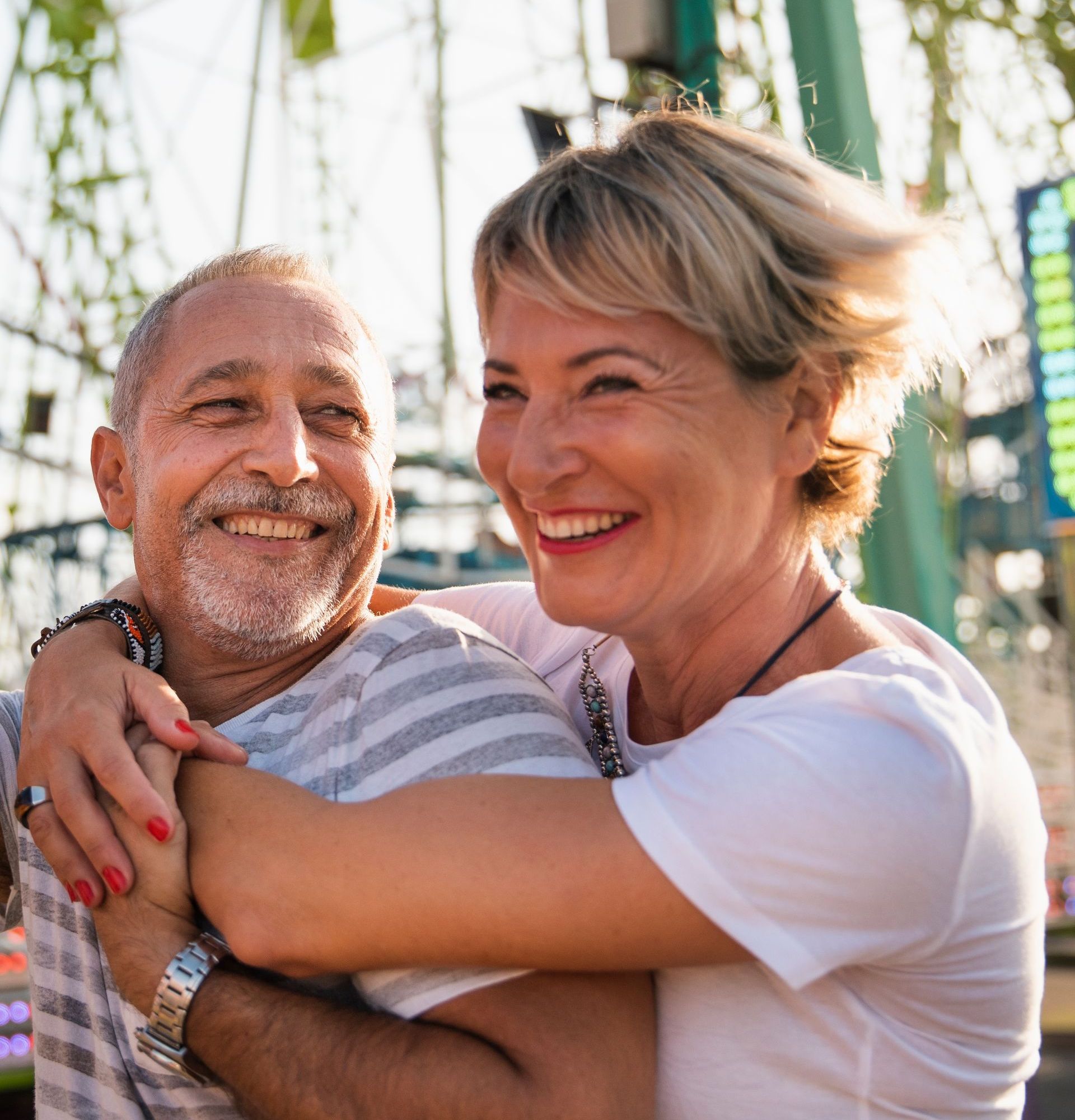Smiling couple embracing at an amusement park; woman with arms around man.