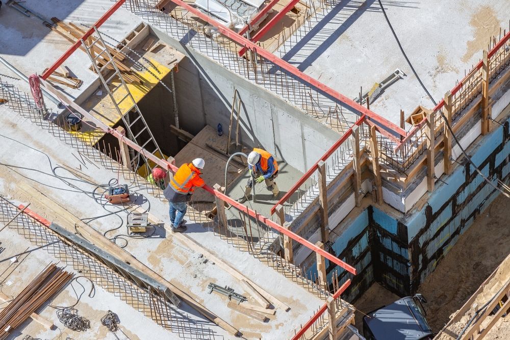 Construction workers in orange vests working on a concrete structure. Building site with wooden framework and tools.